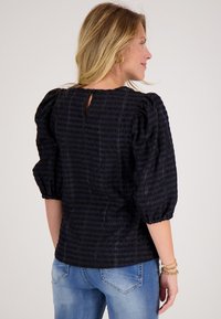 Zwarte blouse van textuur met puffed korte mouwen en een keyhole achterkant detail. Gepaard met lichtblauwe denim jeans.