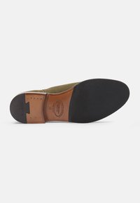Suela de zapatos de ante verde oliva con una inserción de cuero marrón. Presenta goma negra en la parte delantera y acentos metálicos a lo largo de los lados.