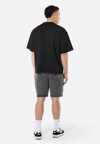 Black oversized t-shirt with short sleeves, paired with gray denim shorts. Model wears white socks and black sneakers; casual streetwear look.
