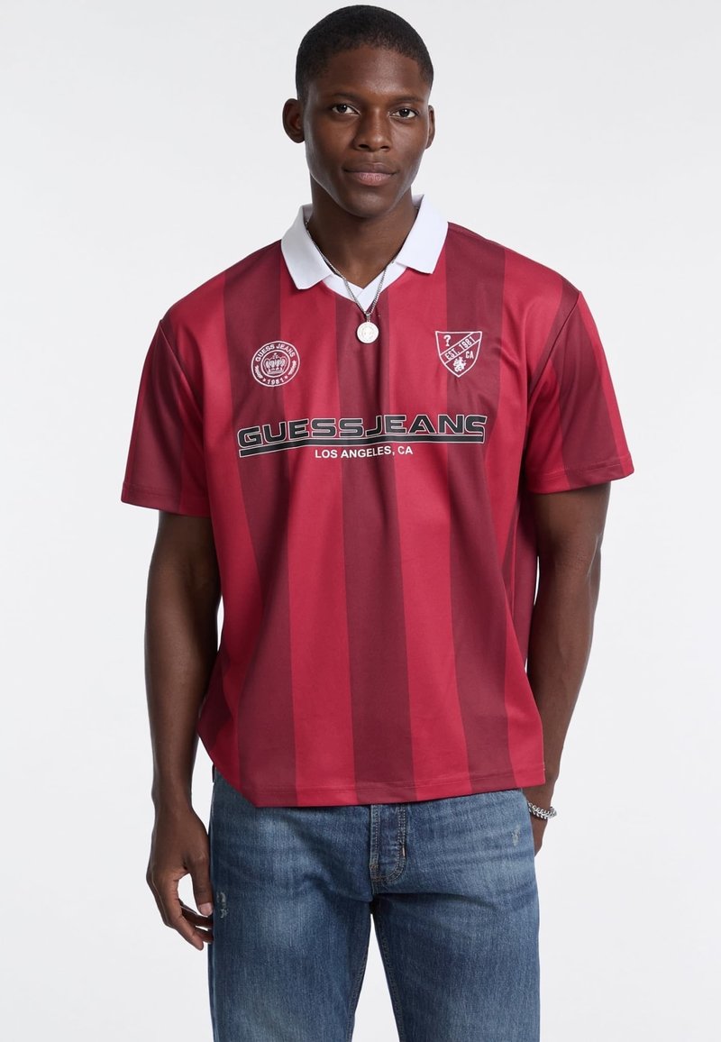 Rot und bordeaux gestreiftes Poloshirt mit weißem Kragen, mit einem Logo und dem Text "GUESS JEANS" in Schwarz auf der Brust.