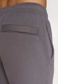 Graue Baumwoll-Jogginghosen verfügen über eine flache Gesäßtasche mit genähtem Rand, einen elastischen Bund und seitliche Taschen. Die Textur ist glatt und weich.