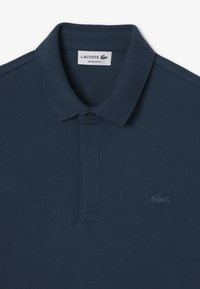 Mörkblå pikétröja med strukturerad tyg, klassisk krage, två-knapps knäppning och en broderad Lacoste-logotyp på bröstet.