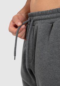 Graue Jogginghose aus weichem Stoff mit elastischem Bund. Verfügt über verstellbare Kordeln und Seitentaschen. Glatte Textur.