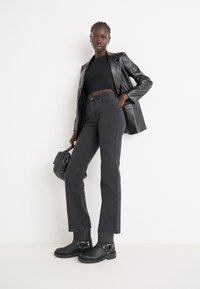 Černé kožené sako přes černý crop top, spárované s tmavými jeansy s vysokým pasem a černými kotníkovými botami s přezkami.