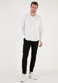 Fehér, hosszú ujjú vászon ing, gombos gallérral és mellzsebbel, fekete slim-fit nadrággal és fehér sportcipővel párosítva.