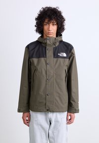 Olijfgroene waterdichte jas met zwarte schouderpanelen, knoopsluiting aan de voorkant, verstelbare capuchon en ritszakken aan de zijkant. Het logo van The North Face is zichtbaar.
