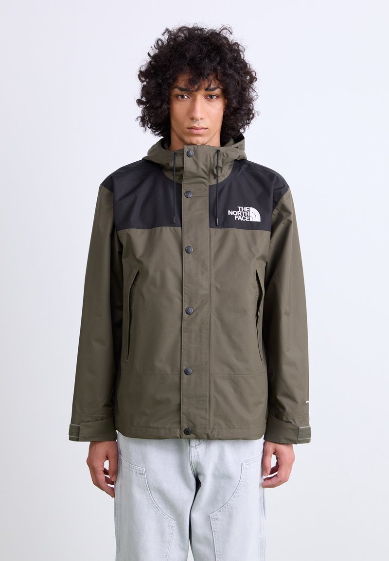 Olijfgroene waterdichte jas met zwarte schouderpanelen, knoopsluiting aan de voorkant, verstelbare capuchon en ritszakken aan de zijkant. Het logo van The North Face is zichtbaar.