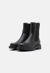Botas de cuero negro hasta el tobillo con detalles de tachuelas a lo largo de las costuras, paneles laterales elásticos y suelas resistentes. Textura suave y diseño robusto.
