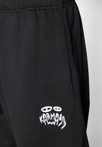 Schwarze Sweatpants aus einem Baumwoll-Mischgewebe, mit einem Kordelzugbund und einem weißen bestickten "KARMA88"-Logo an der Seite.