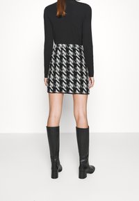 Černý top s dlouhým rukávem v kombinaci s mini sukní s šedým a černým vzorem houndstooth. Černé kozačky na vysokém podpatku k kolenům dotvářejí celkový vzhled.