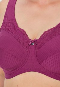 Mauve podprsenka s krajkou a malou mašlí uprostřed, s texturovanou tkaninou a širokými ramínky pro oporu.