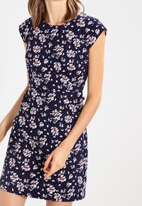 Navy floral dress with cap sleeves, featuring a fitted waist and scattered white and red floral patterns. Soft fabric with slight texture.