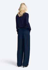 Pullover blu navy a maniche lunghe abbinato a pantaloni blu navy a vita alta. I pantaloni presentano un design a gamba larga e una sottile trama.