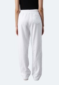 Weiße, locker sitzende Sweatpants aus weicher Baumwolle, mit einem elastischen Bund und einer einzelnen Gesäßtasche. Glatte Textur mit einem lässigen Design.