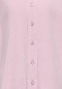 Chemise boutonnie rose clair en tissu texturé, avec six boutons assortis sur le devant et une finition douce et lisse.