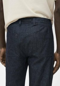 Donkerdenim broek met een rechte snit, voorzien van twee achterzakken en een klassieke tailleband. De stof heeft een gestructureerde afwerking.