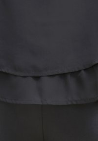 Tissu noir à plusieurs couches avec des coutures visibles et de légers plis créant un détail de bordure froncée.