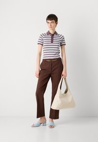 Polo a righe marrone e bianco, pantaloni marroni con cintura a catena, mule con tacco azzurro chiaro e borsa a spalla beige.