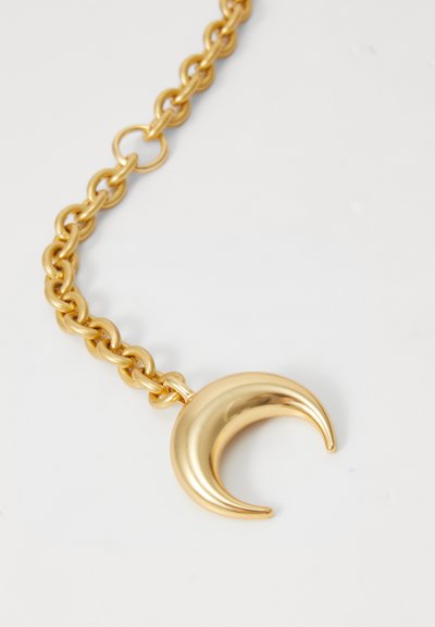Collar de cadena dorada con un colgante en forma de luna creciente. El colgante tiene una superficie lisa y brillante, y una forma curvada.