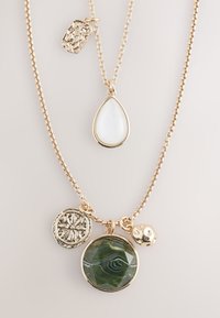 Gold-tone layered necklace featuring a teardrop white stone, green patterned agate, decorative metal charm, and textured round pendant.