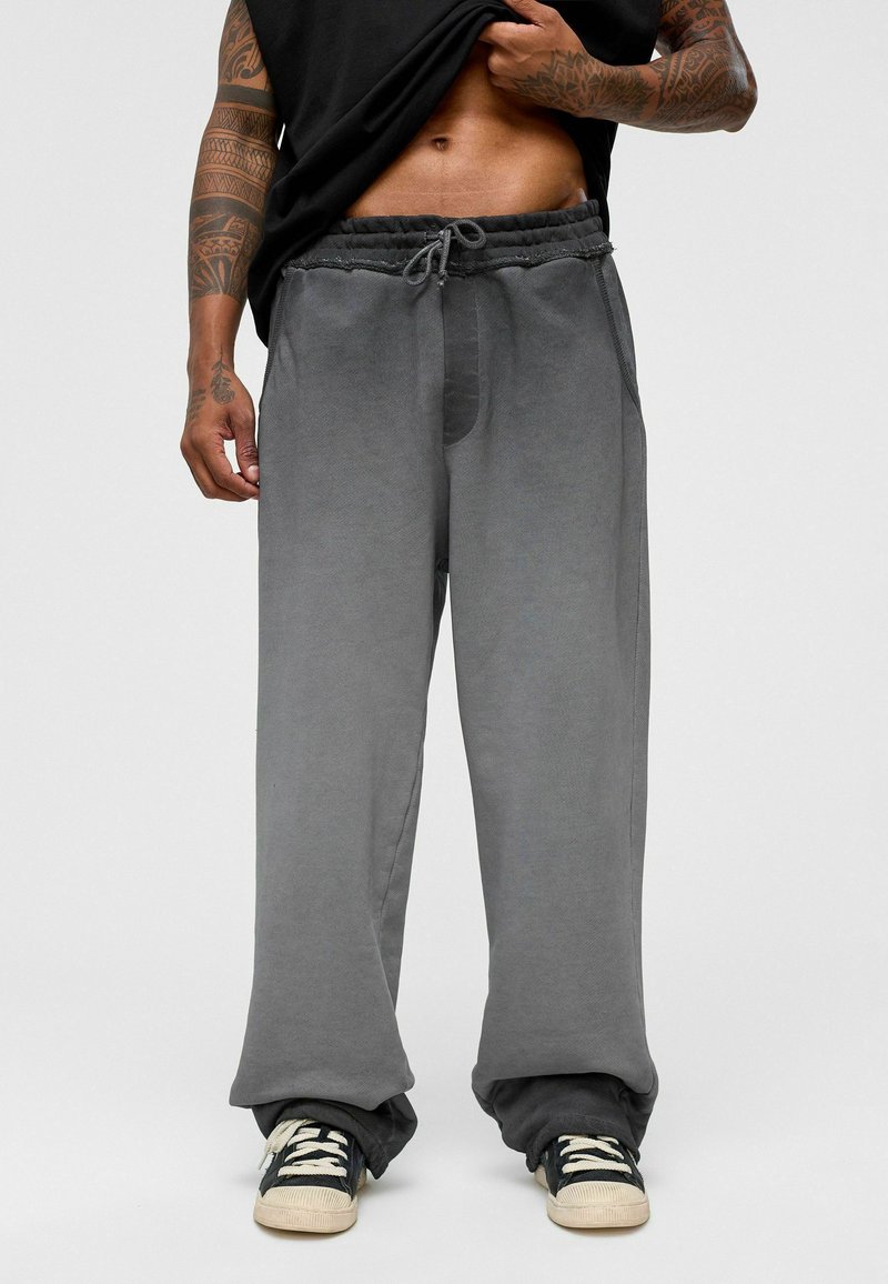Grijze sweatpants met een losse pasvorm, een trekkoord in de taille, zijzakken en een gestructureerde stof, gecombineerd met zwarte sneakers.