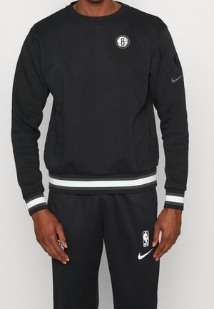 Sweatshirt noir à col rond, logo de l'équipe sur la poitrine et poignets rayés. Fabriqué en tissu doux, il présente une coupe décontractée et un design minimal.