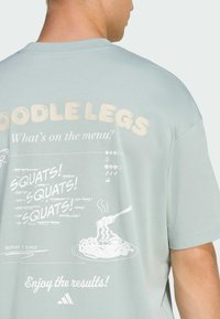 Light green cotton t-shirt featuring a graphic with white text and illustrations of noodles and exercises on the back. Crew neckline, short sleeves.
