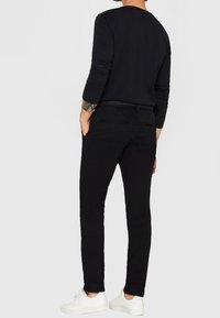 Chemise noire à manches longues, pantalon noir ajusté et baskets blanches. Design simple avec une texture lisse, sans motifs ou accents visibles.