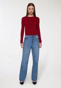 Czerwona bluzka z długim rękawem w połączeniu z jasnoniebieskimi spodniami z wysokim stanem i szerokimi nogawkami. Czarne buty na szpilkach dopełniają wygląd. Gładka faktura i dopasowany krój.