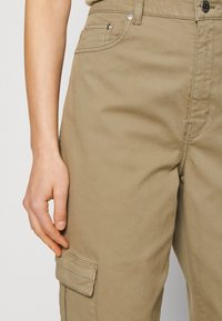 Khaki cargo kalhoty mají hladkou texturu, pět kapes a boční kapsu na cargo. Materiál je z bavlny s odolným povrchem.