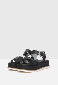 Sandalias de plataforma negras hechas de cuero suave. Cuentan con tiras entrecruzadas, un acento de hebilla plateada y una suela de goma texturizada.