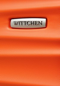 Pomarańczowy materiał o teksturze z diagonalnym wzorem pasków, z wyraźnie umieszczonym odznaką logo "WITTCHEN" w kolorze srebrnym.