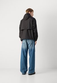 Zwarte hoodie met een textuurpatroon, gecombineerd met losse blauwe jeans. De outfit heeft casual, oversized silhouetten.