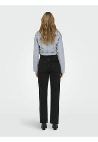 Chaqueta de mezclilla cortada en azul claro combinada con pantalones de tela negra de tiro alto y pierna recta. Tejido texturizado con detalle de dobladillo deshilachado, bolsillos frontales visibles.