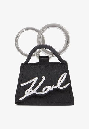Črn usnjen ključenka v obliki ročne torbice, opremljena s srebrnim logotipom "Karl" in dvema srebrnima obročkastima ključema. Teksturirana površina s šivi.
