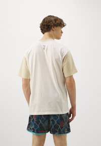 Tricou cu guler rotund, în nuanțe de alb murdar și bej, fabricat din bumbac moale. Prezintă mâneci în contrast și un logo mic pe spate.