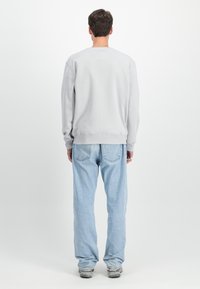 Felpa grigio chiaro con scollatura rotonda e polsini a coste, abbinata a jeans blu chiaro. Il tessuto sembra morbido con minimal dettagli.