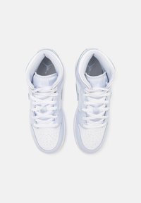 Pár bielych vysokých tenisiek s šnúrkami, perforovaným špičkou a viditeľným logo Jumpman v oblasti päty na jednofarebnom pozadí.