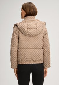 Beżowa kurtka puchowa z wzorzystą powierzchnią, kapturem i elastycznym wykończeniem u dołu. Posiada teksturowane wykończenie oraz zamek błyskawiczny z przodu.