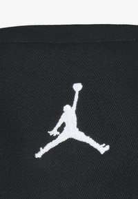 Svart stoffcaps med en hvit brodert Jumpman-logo i midt i en luftposisjon, med en teksturert overflate og strukturert design.