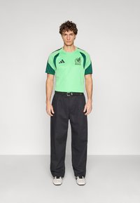Green and black adidas sports jersey features a textured design and logo, paired with loose-fitting black trousers and white sneakers.