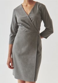 Grå knälång klänning med V-ringning, trekvartsärmar och draperad frontdetalj. Tyget verkar slätt med en svag lyster.