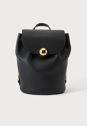 Zaino in pelle nera con patta e grande chiusura a bottone rotondo dorato, mostrato su sfondo bianco.
