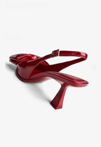 Rdeče patent usnjene slingback čevlje s konicami, cvetličnim detaljem in sculptiranim kvadratnim peto. Nastavljiv gleženjski trak z metalno zaponko.