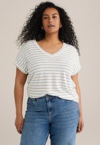 T-shirt a maniche corte a V bianca e beige a righe, realizzata in un tessuto morbido, abbinata a jeans blu a vita alta. Vestibilità casual e design rilassato.