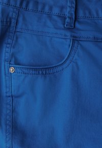 Blaue Stoffhose mit glatter Textur, ausgestattet mit einer Vordertasche mit silbernem Knopfdetail und sichtbaren Nähten.