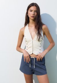 Top cropped a halter cream con dettagli a bottoni, abbinato a pantaloni corti blu scuro con coulisse. Tessuto dalla texture liscia, design minimalista.