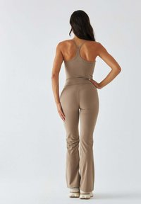 Tan athletic outfit with a fitted tank top and flared pants. The material is smooth, stretchy, and hugs the body with a minimal design.