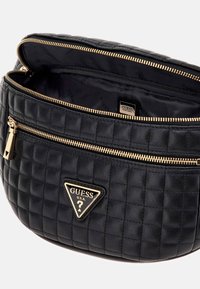 Pochette trapuntata nera con logo Guess e zip dorata, leggermente aperta che mostra l'interno rivestito in nero con il logo Guess.
