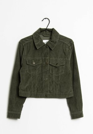 Oliwkowa kurtka sztruksowa o kroju cropped z zapięciem na guziki z przodu, dwoma kieszeniami na piersi, kołnierzem i długimi rękawami na czarnym wieszaku.